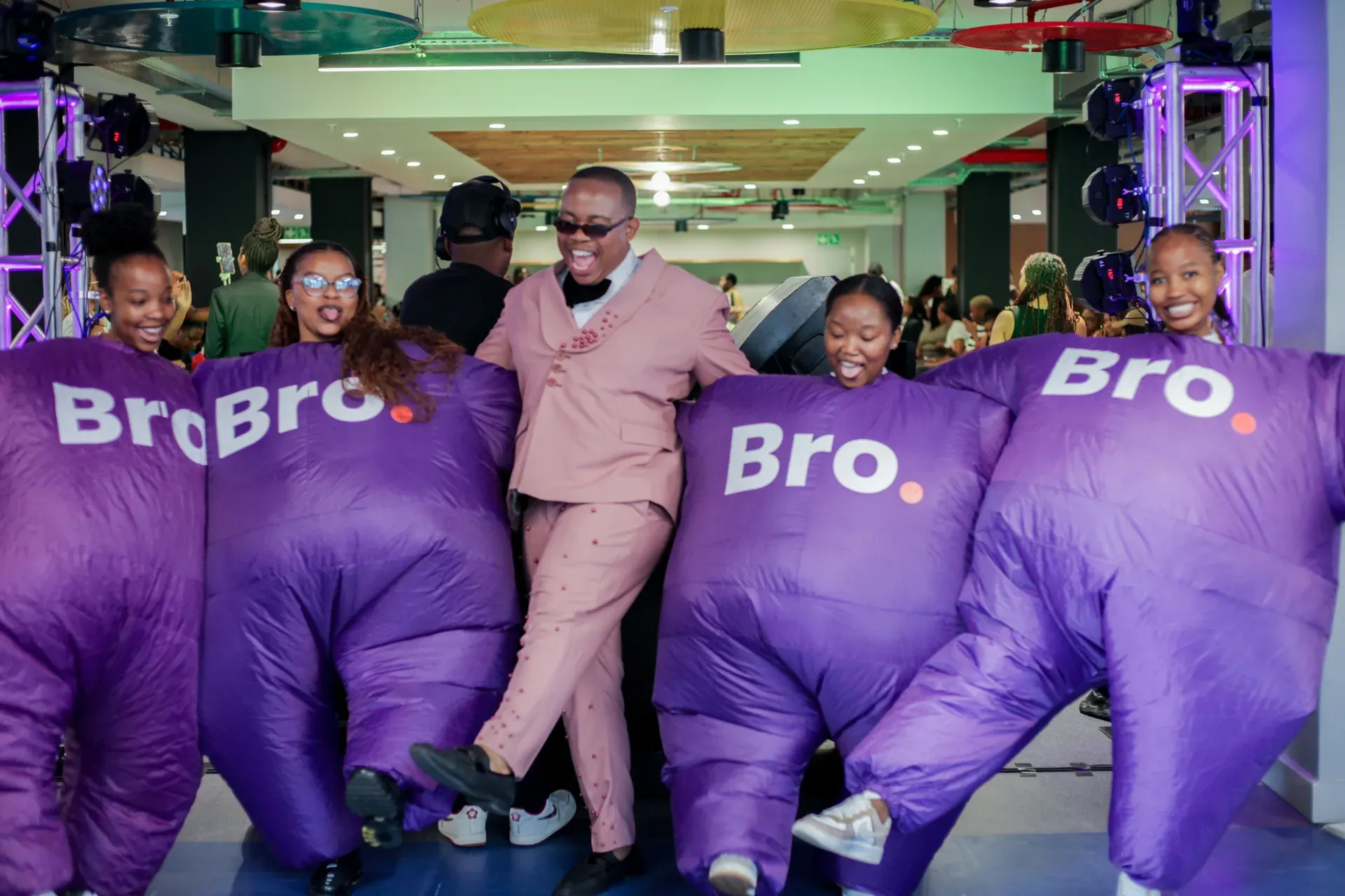 Man in a pink suit dancing with Bro mascots at Rosebank College